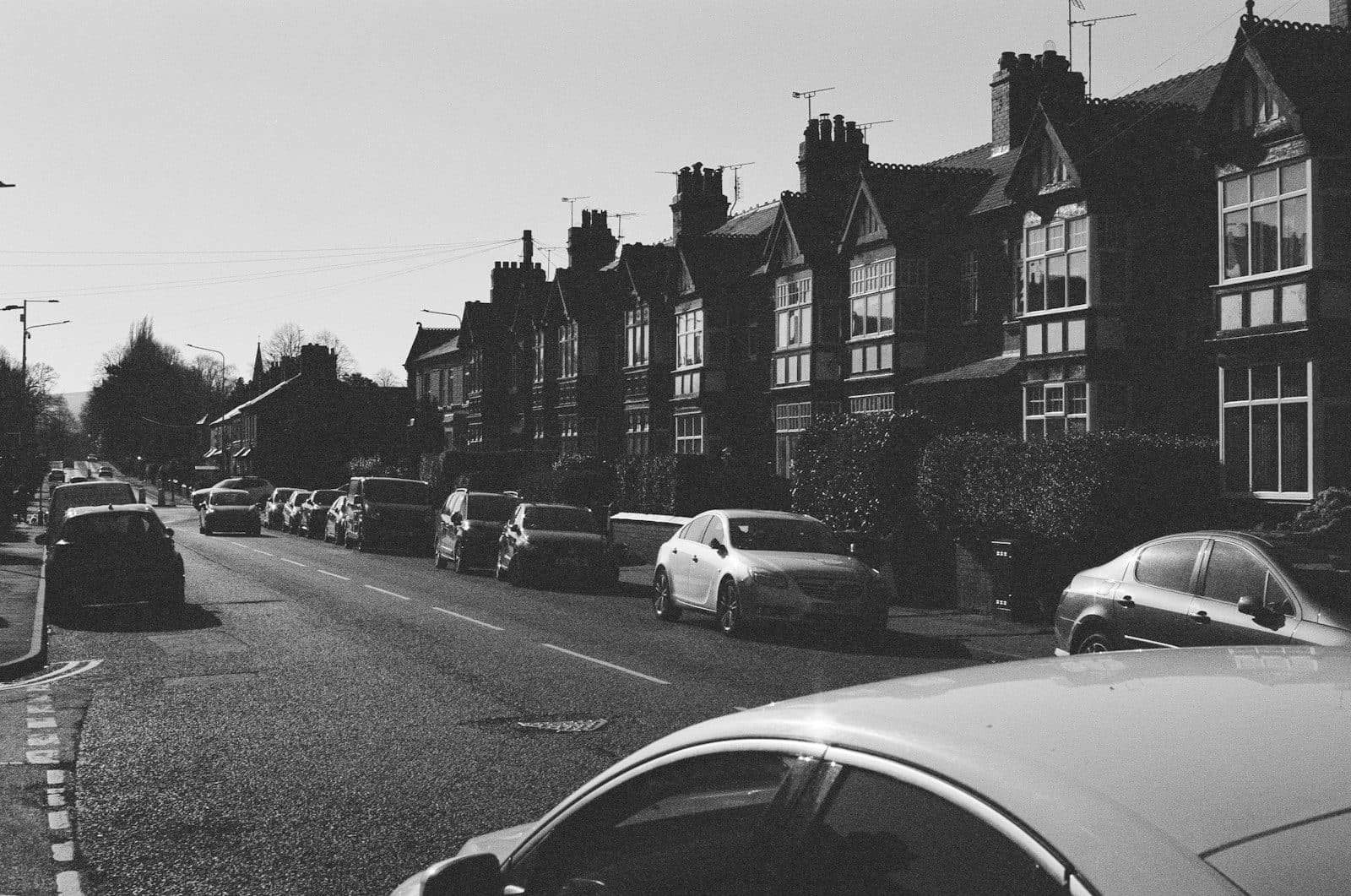 A residential street in Wrexham lined with parked cars and Victorian houses